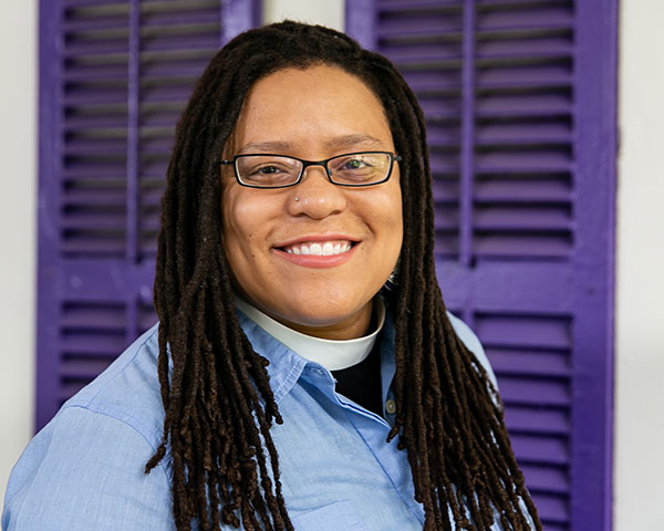 Kim smiling and standing in front of a home with purple shutters