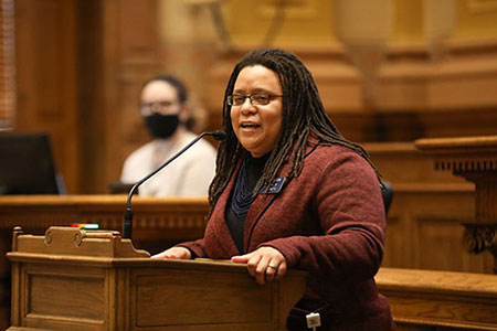 Kim with her hands on a podium delivering a speech in the senate